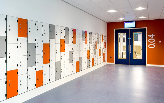 orange white and grey wall lockers on a white wall with a blue double door ahead of them on an orange wall